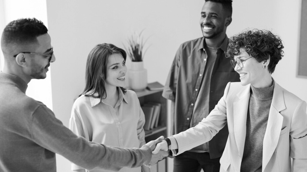 Un homme et une femme se serrent la main, le sourire aux lèvres, tandis qu'un autre homme et qu'une autre femme sont derrière eux et les regardent également en souriant.