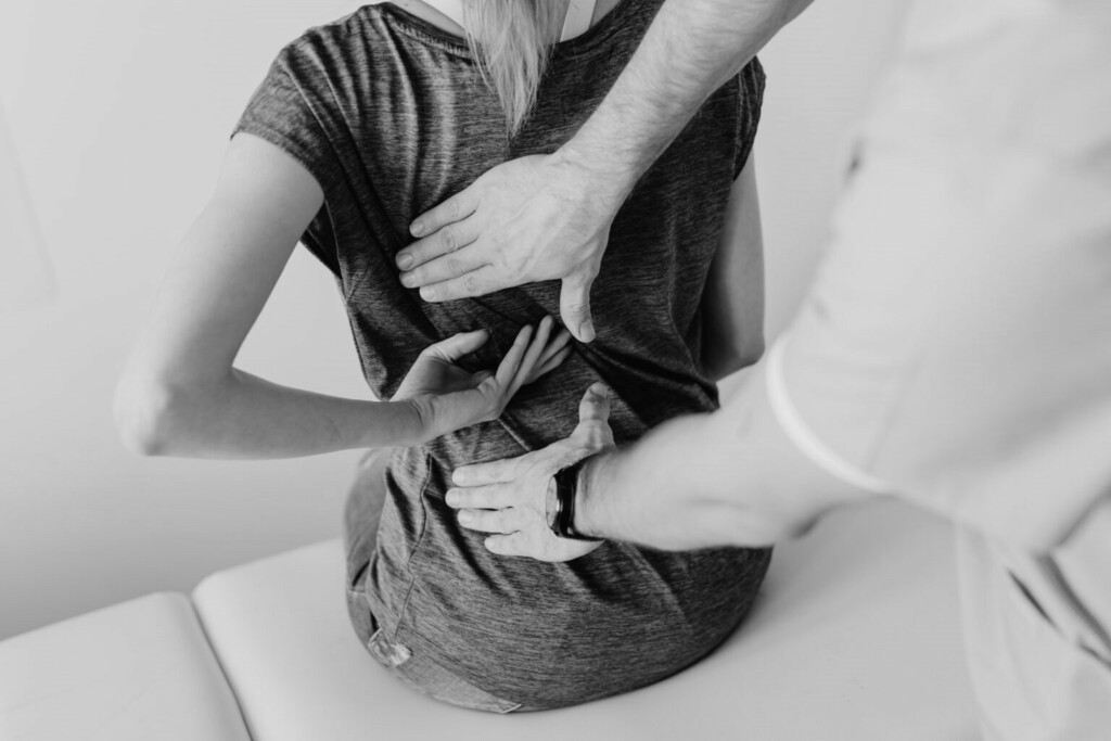 Une femme ayant mal au dos du à une mauvaise posture et se faisant ausculter par un médecin.